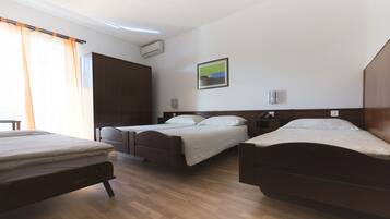 Une chambre d’hôtel avec trois lits en bois, une armoire, un appareil de climatisation et un tableau au mur.