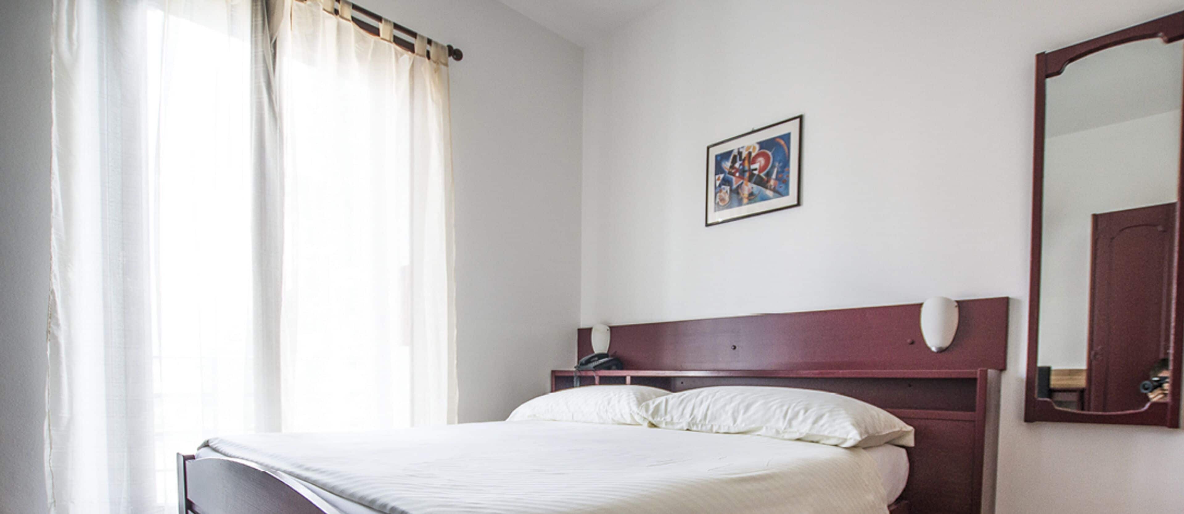 A bedroom with a bed, a headboard, a bedside table, a mirror, and a wall-mounted picture.