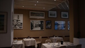 Un restaurant où les tables sont dressées pour le service, où des tableaux encadrés ornent les murs et où le plafond est décoré de panneaux en bois.