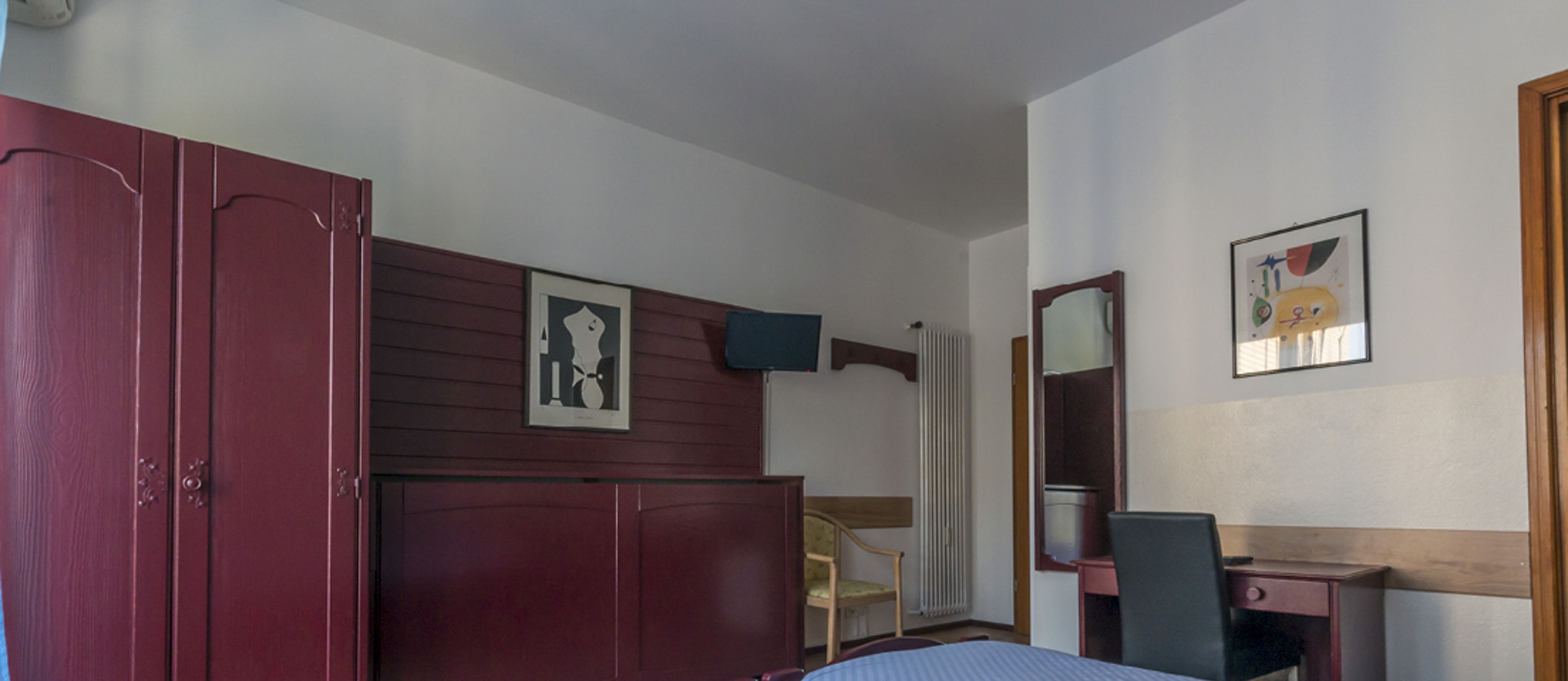 A room with a bed, a desk, a chair, a wardrobe, and a radiator.