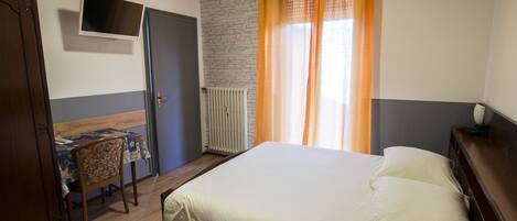 A bedroom with a bed, a desk, a television, and a window with curtains.
