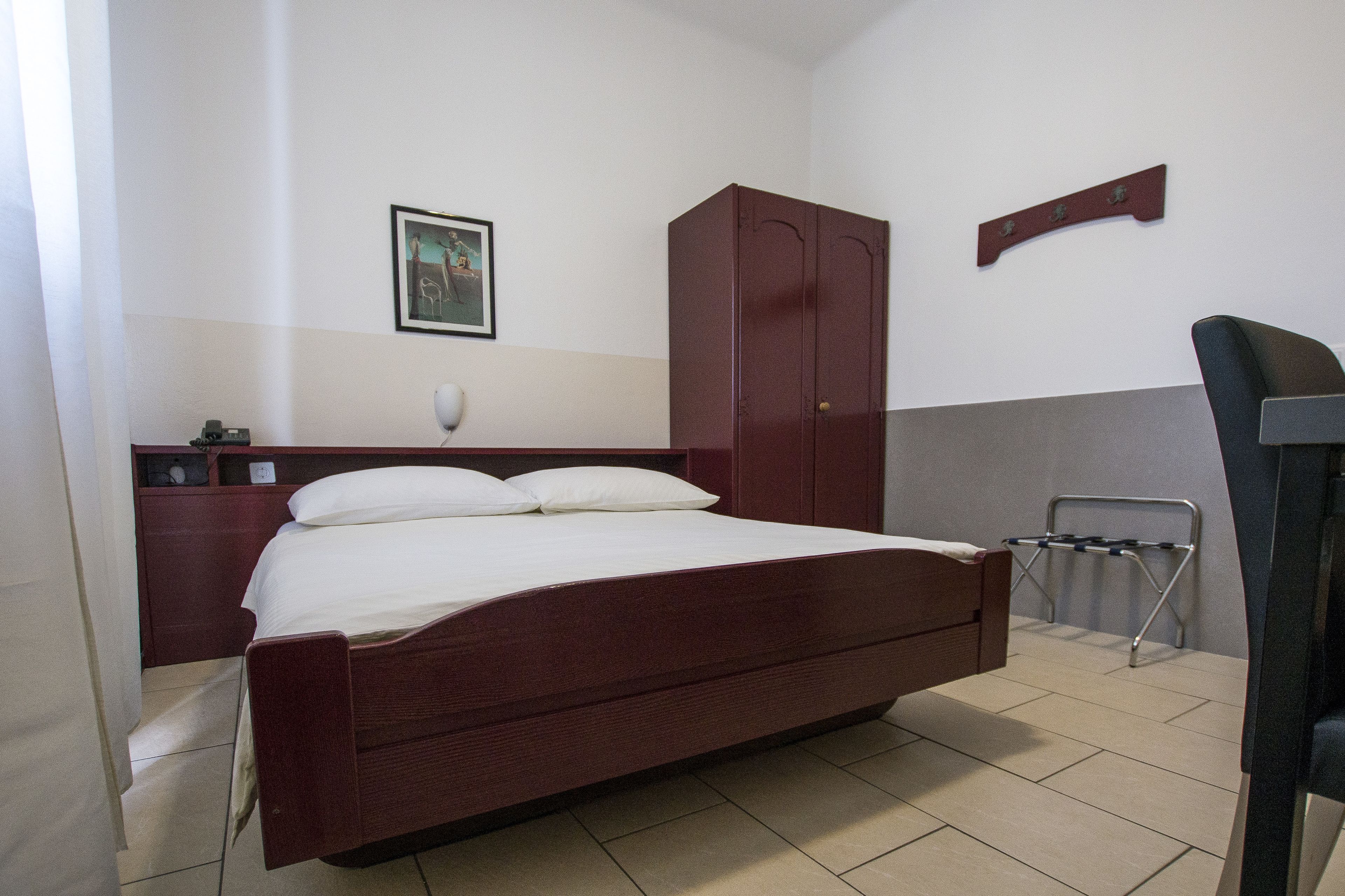A bedroom with a wooden bed, a nightstand, a wardrobe, a wall-mounted shelf, and a hanging laundry rack.