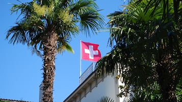 A building with a flag, palm trees, and a clear blue sky.