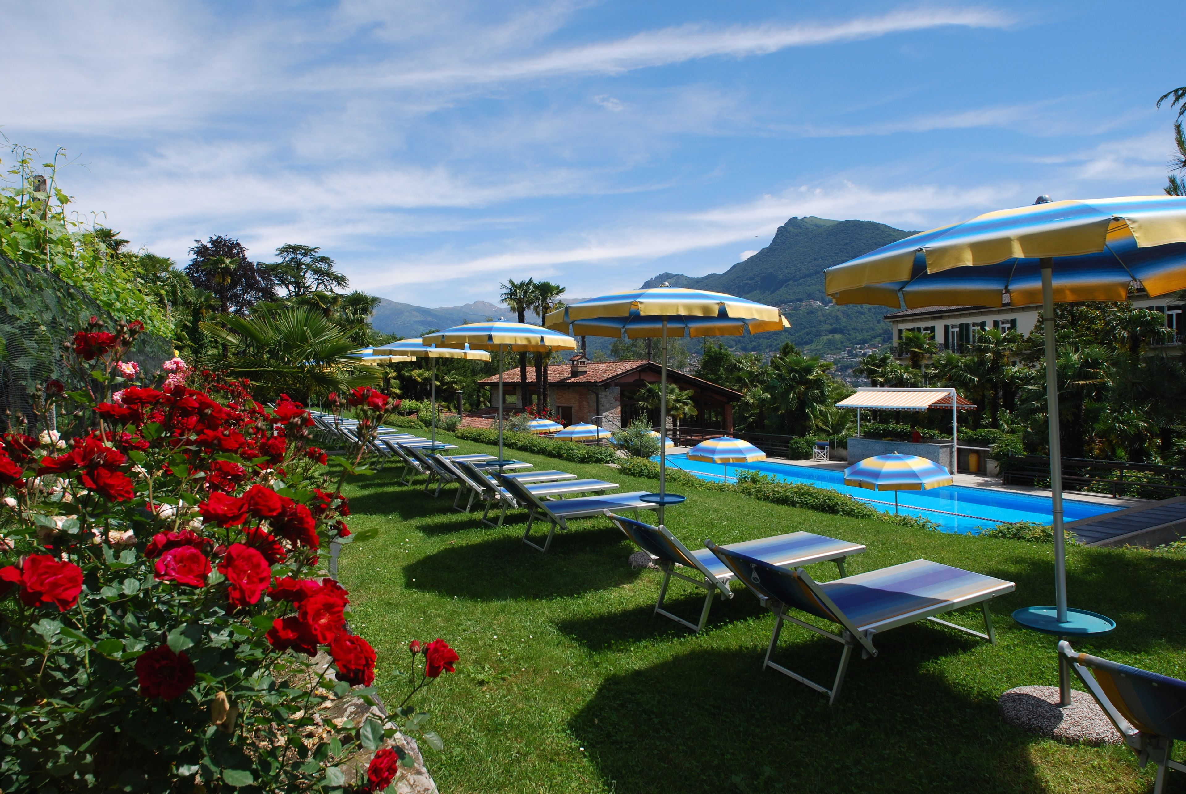 Un espace aménagé au bord de la piscine, avec des chaises longues et des parasols, entouré d’une végétation luxuriante et dominé par une chaîne de montagnes.