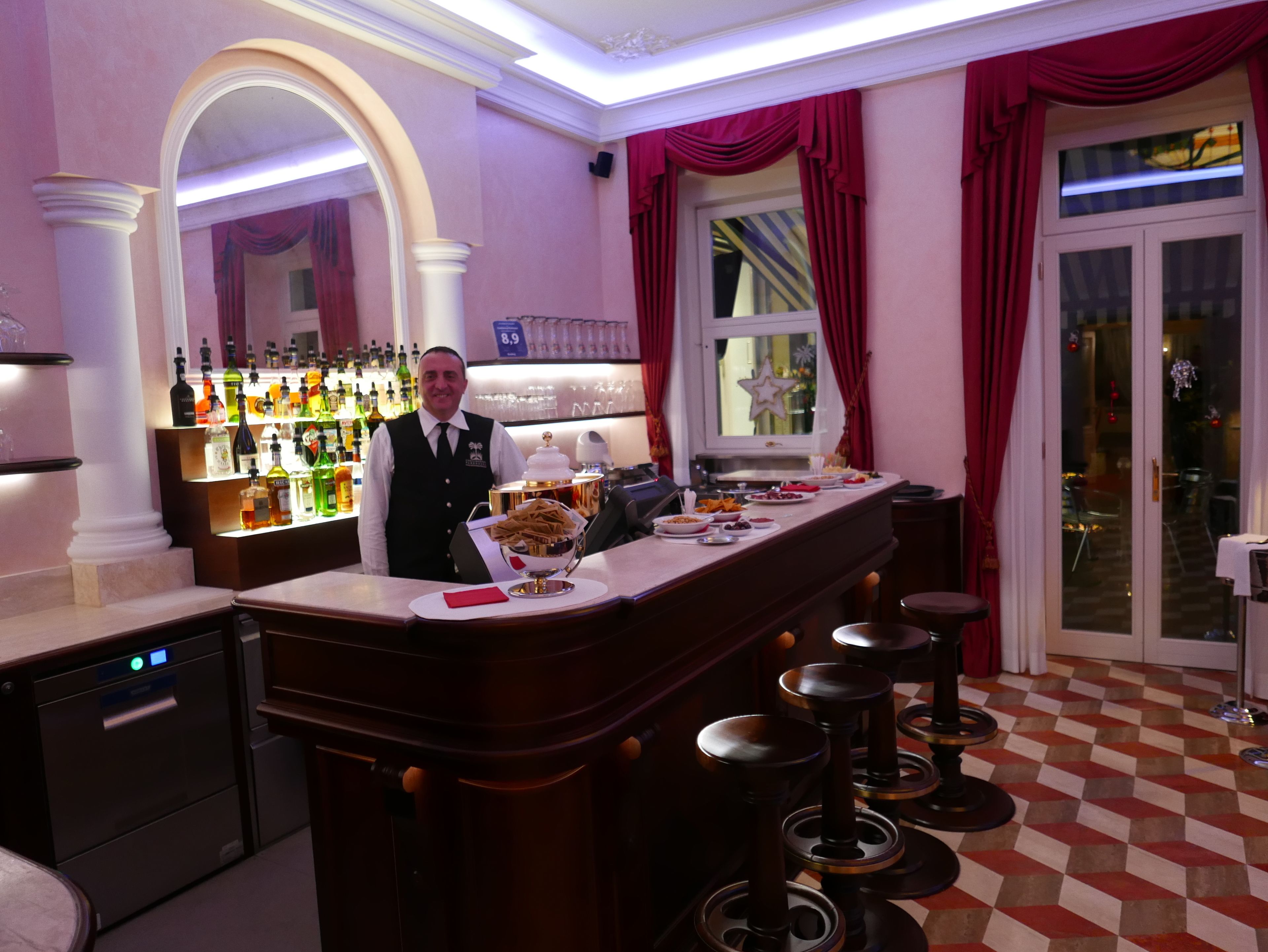 Eine Bar mit Bartender, einer Theke mit Snacks und einem Schachbrettmuster-Boden.