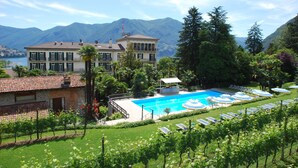 A large building with a swimming pool and sun loungers, surrounded by lush greenery and mountains in the background. - Continental Parkhotel (Lugano)