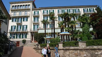 A multi-story hotel with balconies, a stone wall, and palm trees.
