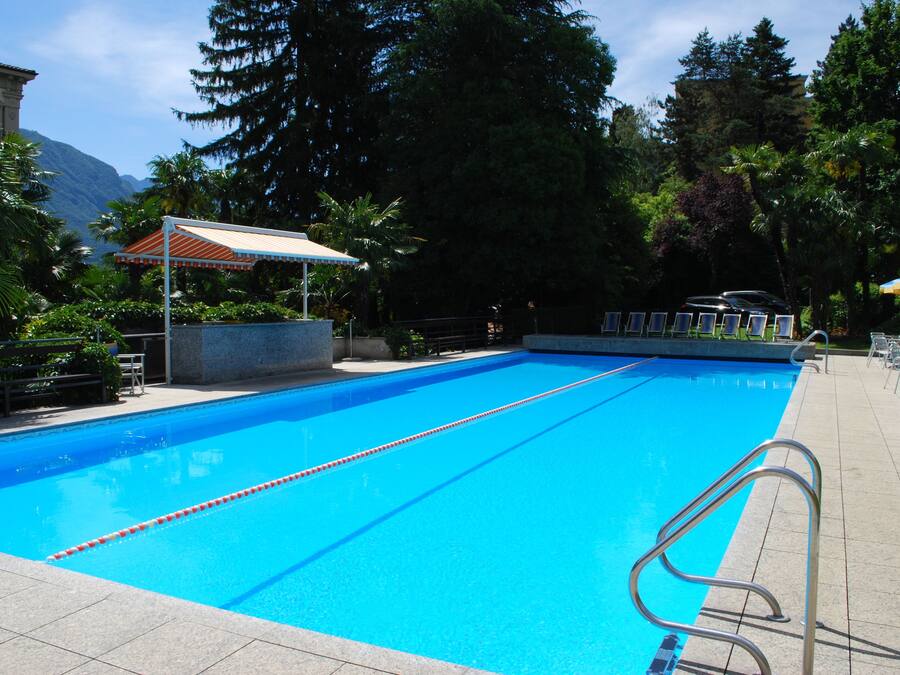 Piscina azul cristalina con una silla de salvavidas y una zona sombreada.