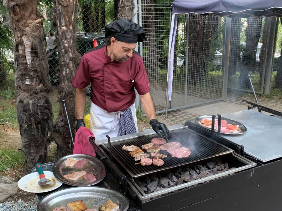 A person grilling meat outdoors with a grill and a tent in the background.