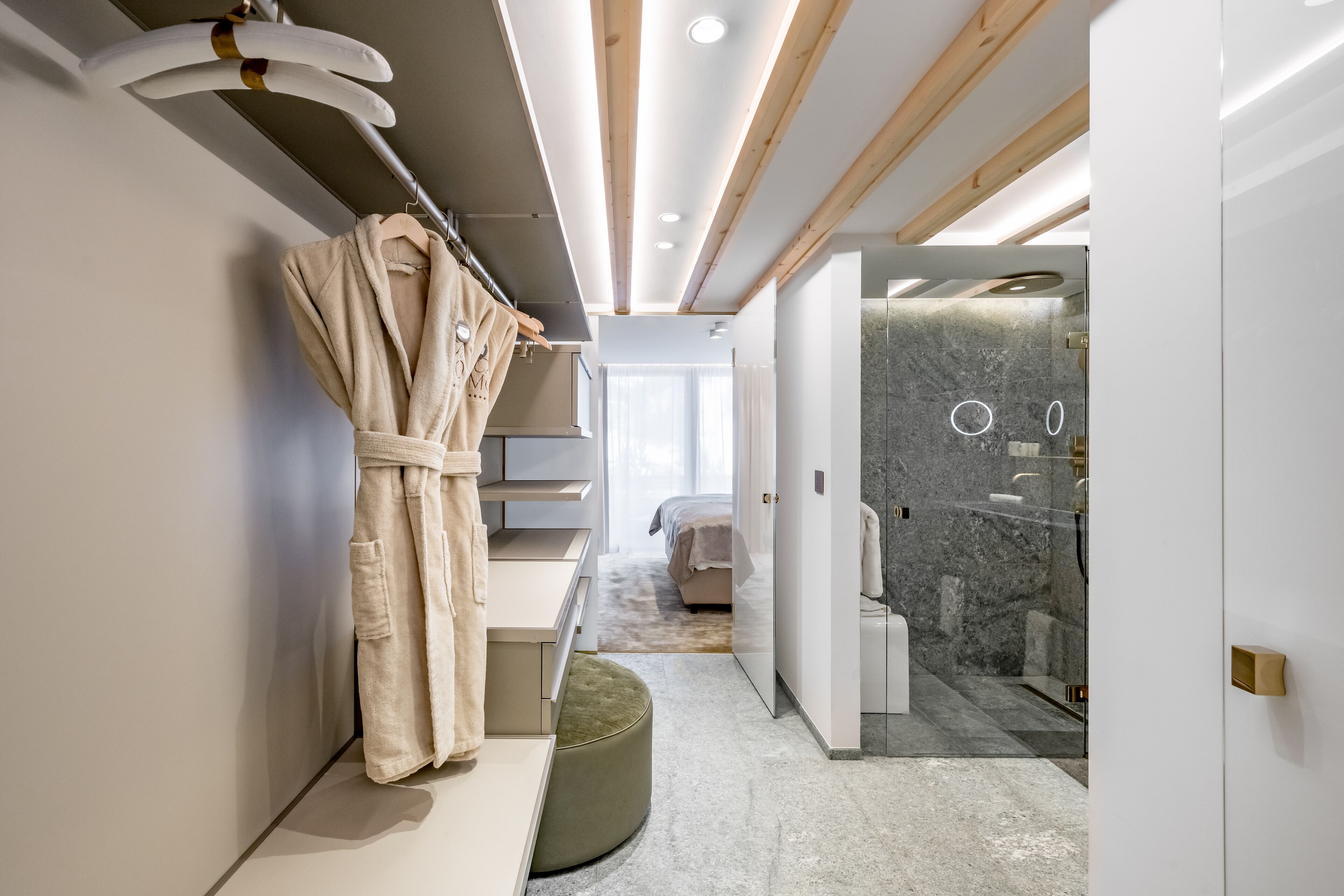 Ein modernes Badezimmer mit bodenebenen Dusche, einem Bademantel auf einem Haken und einem Bett im Hintergrund.