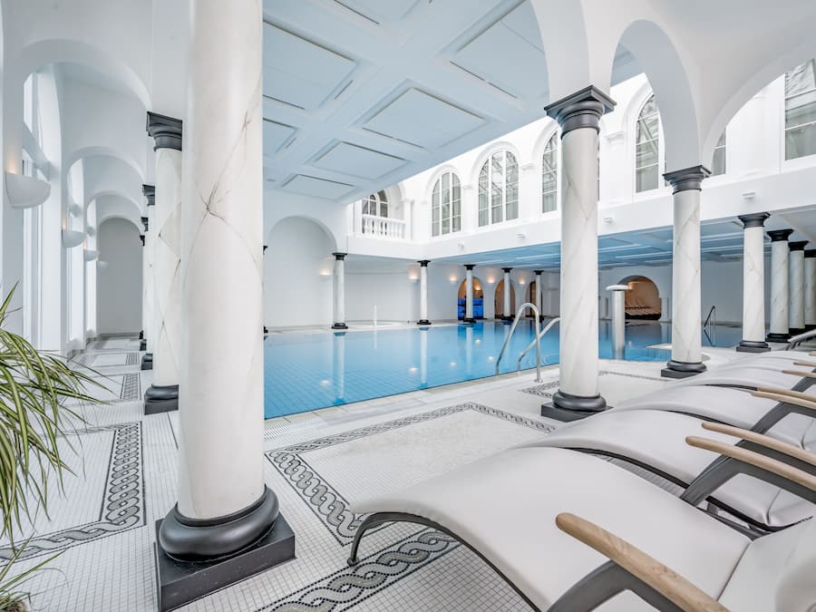 Ein geräumiger, überdachter Pool mit weißen Säulen und Fliesenboden.