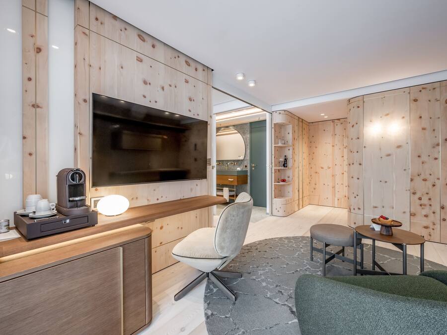 Una habitación de hotel moderna con un panel de pared de madera, un televisor de pantalla plana, una cafetera, un sofá cómodo y una pequeña mesa de comedor.