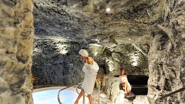 Un área de spa con paredes de piedra, un jacuzzi y una persona sentada junto a él.
