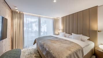 Une chambre moderne avec un grand lit, un mur d’accent en bois, une télévision et une grande fenêtre avec des rideaux.
