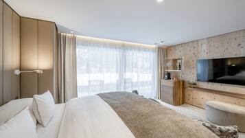 Ein modernes Hotelzimmer mit einem großen Bett, einem Fernseher, einem Holzkabinett und einem großen Fenster mit Vorhängen.