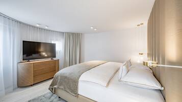 Un dormitorio moderno con una cama grande, un televisor de pantalla plana sobre un tocador de madera y una mesita de noche con lámpara.