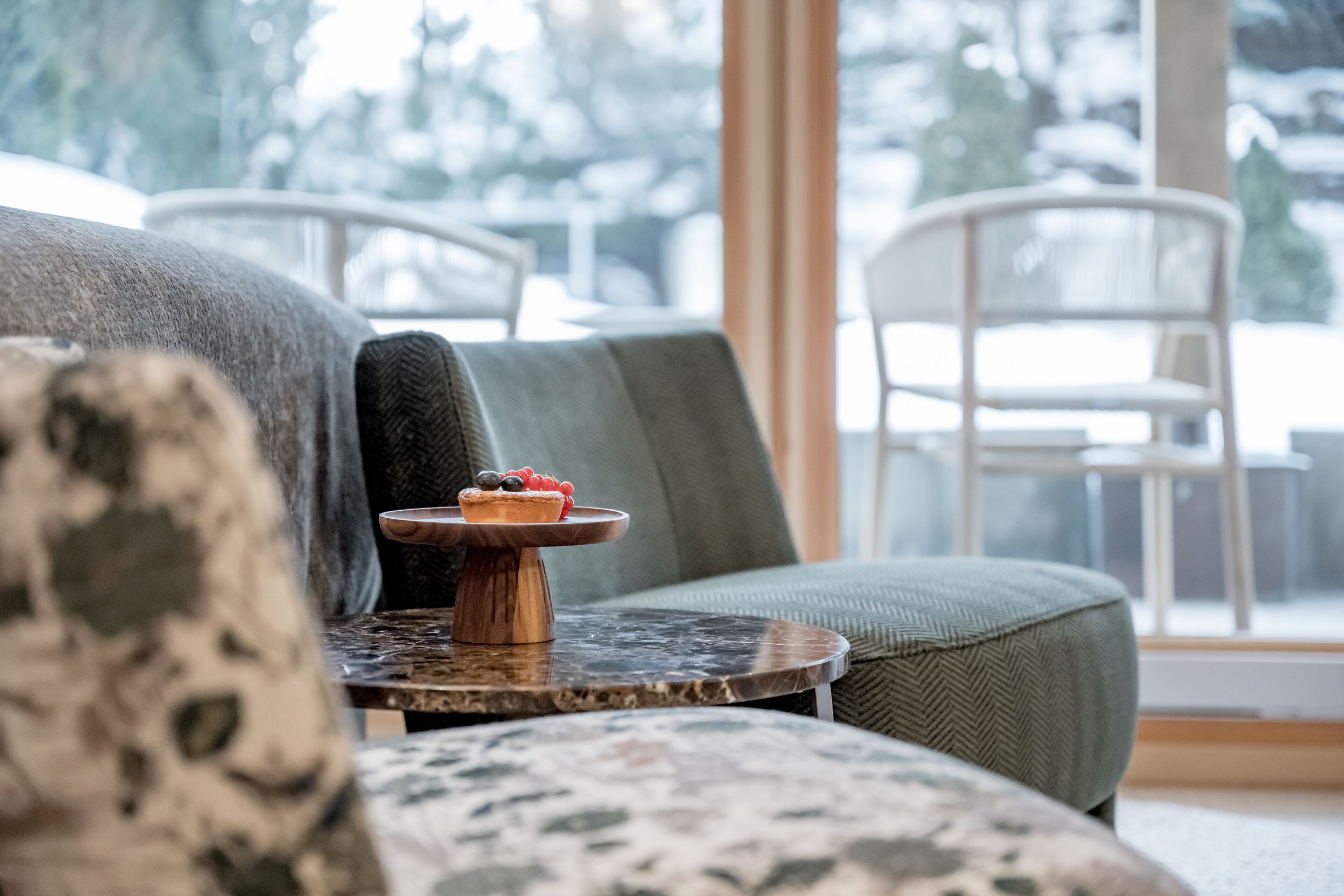 A cozy seating area with a round table featuring a dessert, a green cushioned sofa, and white chairs.