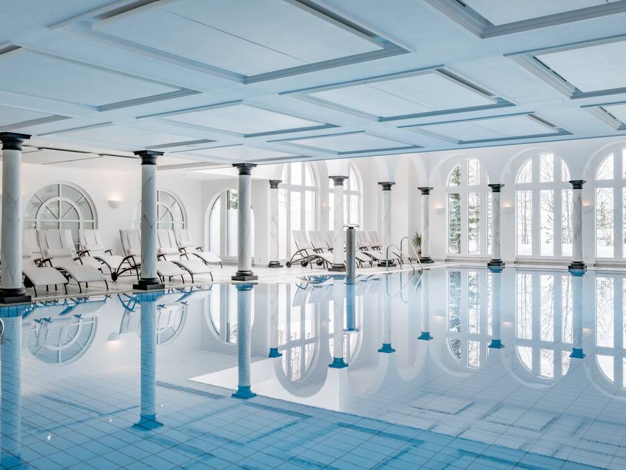 Ein großes Hallenbad mit klaren Spiegelungen, weißen Säulen und bogenförmigen Fenstern.