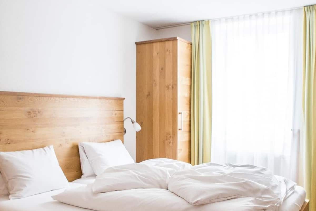 Quarto com estrutura de cama de madeira, roupa de cama branca, guarda-roupa de madeira e luminária no teto.