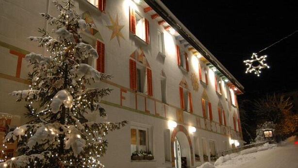 A snow-covered building with a Christmas tree in front. - Hotel Filli (Scuol)