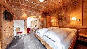 A wooden room with a large bed, a chair, a TV, and a mirror. - Hotel Filli (Scuol)