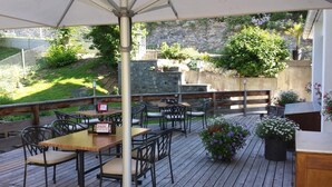 An outdoor patio with wooden tables and chairs, surrounded by a stone wall and greenery. - Hotel Filli (Scuol)