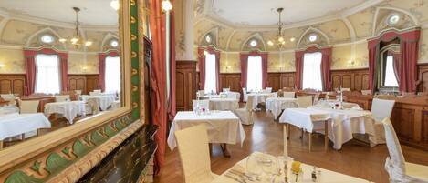 Een statig eetzaal met meerdere gedekte tafels, een vleugelpiano en decoratieve wandornamenten.