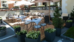 An outdoor patio with tables and chairs, surrounded by potted plants and umbrellas.