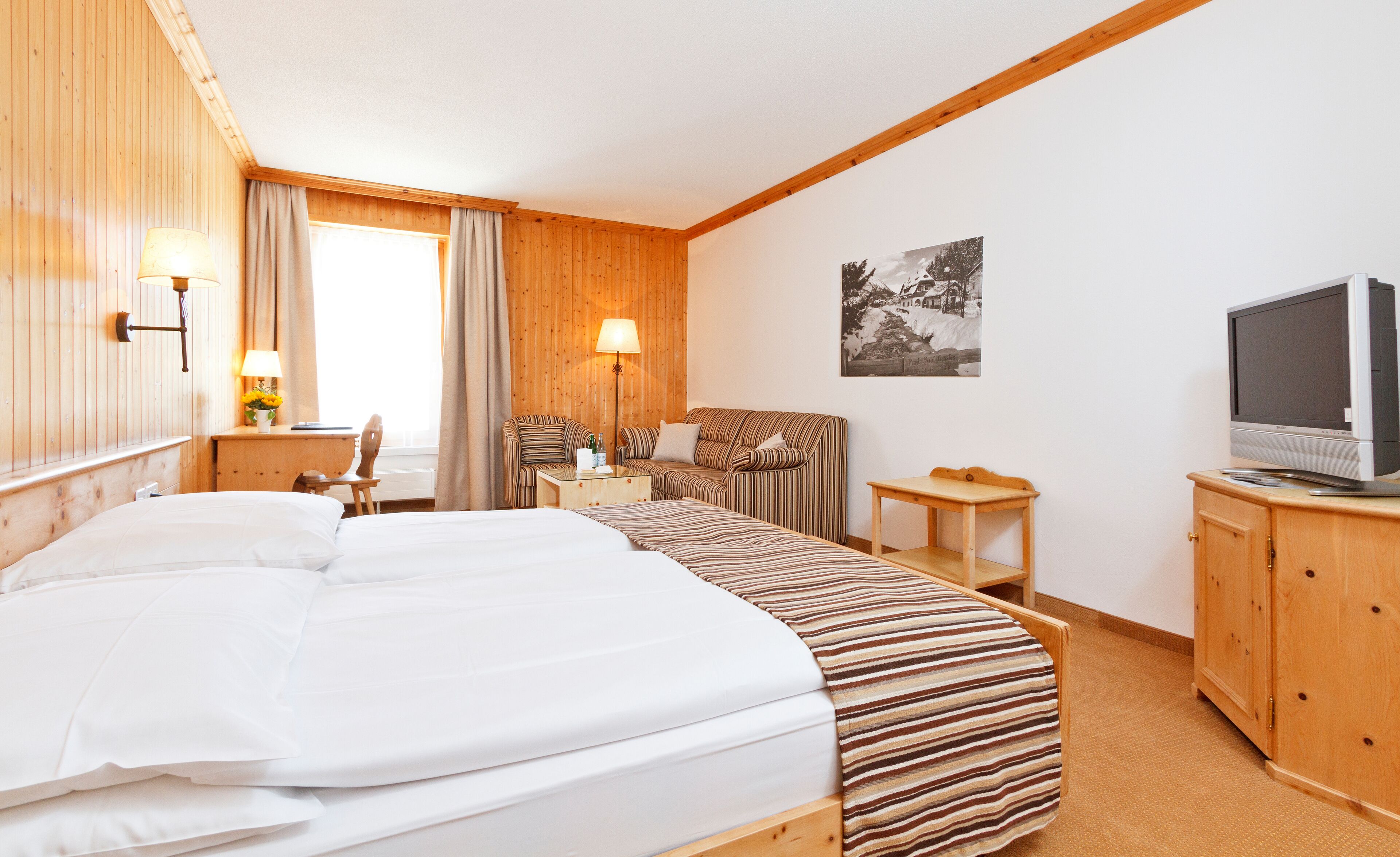Une chambre d’hôtel avec un grand lit, une tête de lit en bois, une télévision et une petite table.