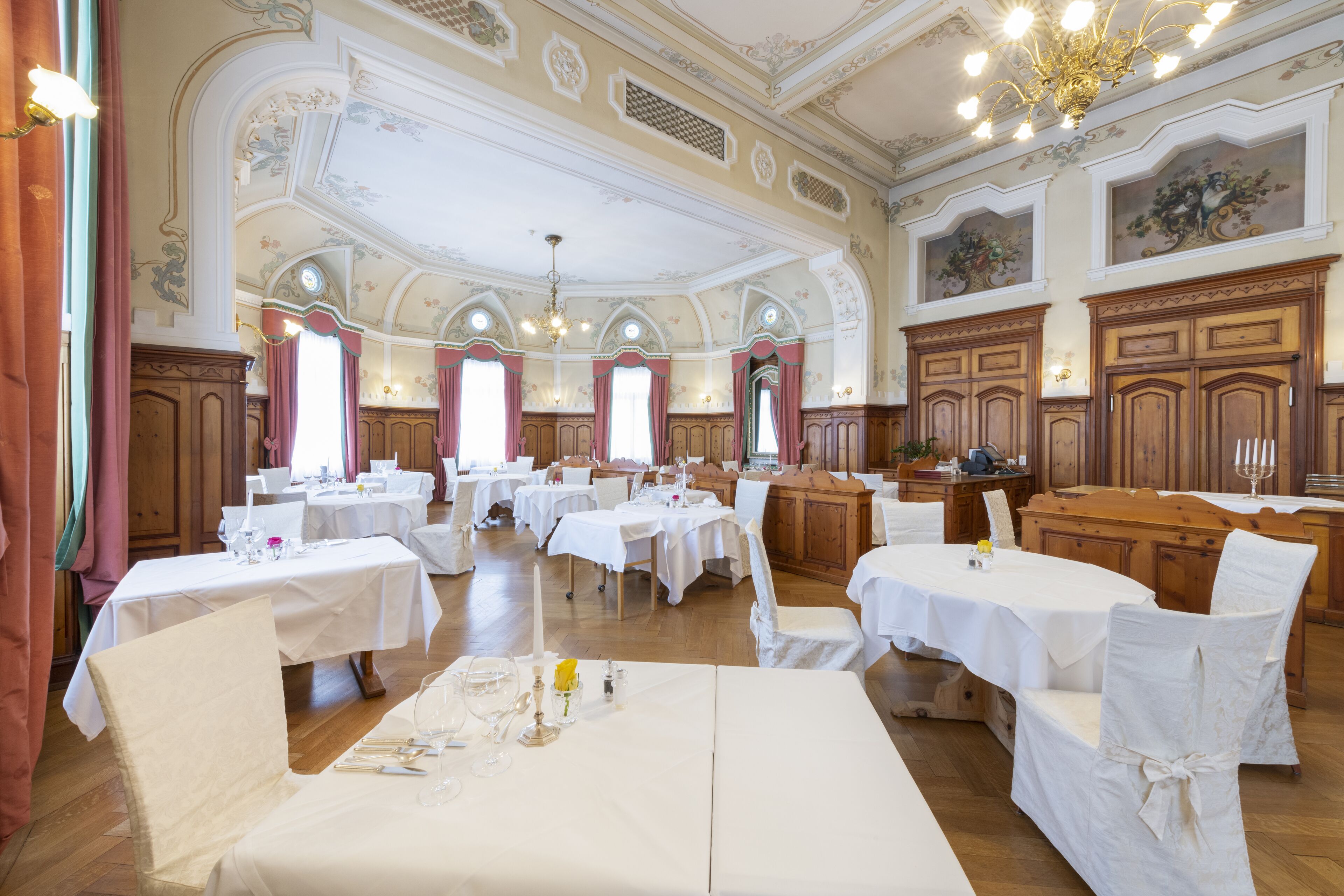 A banquet hall with multiple round tables, white tablecloths, and chairs.