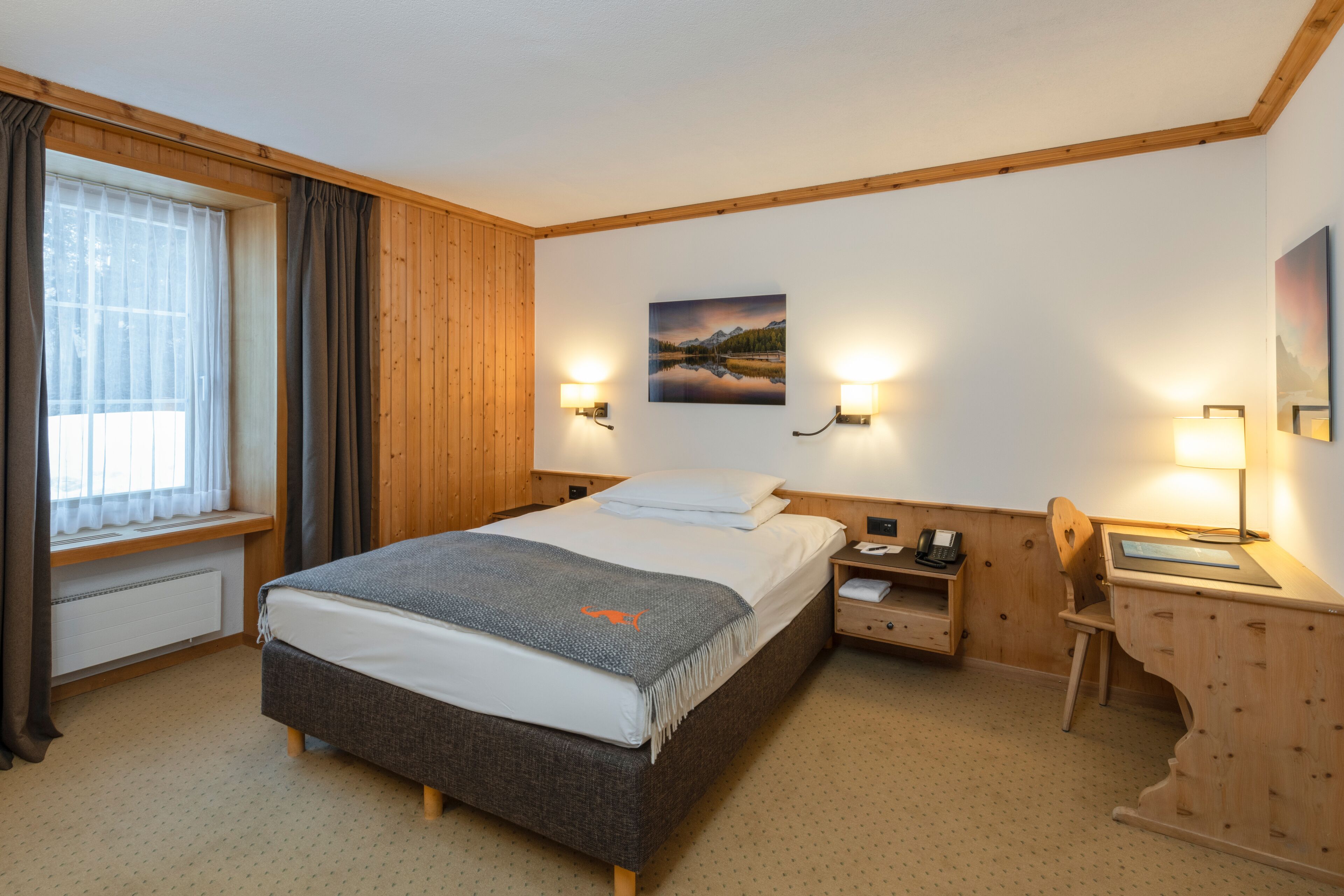 Ein Schlafzimmer mit Bett, Nachttischen, einem Schreibtisch und einem Fenster mit Vorhängen.