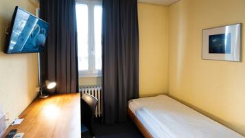 A hotel room with a bed, a desk with a lamp, a TV, and a window with curtains.