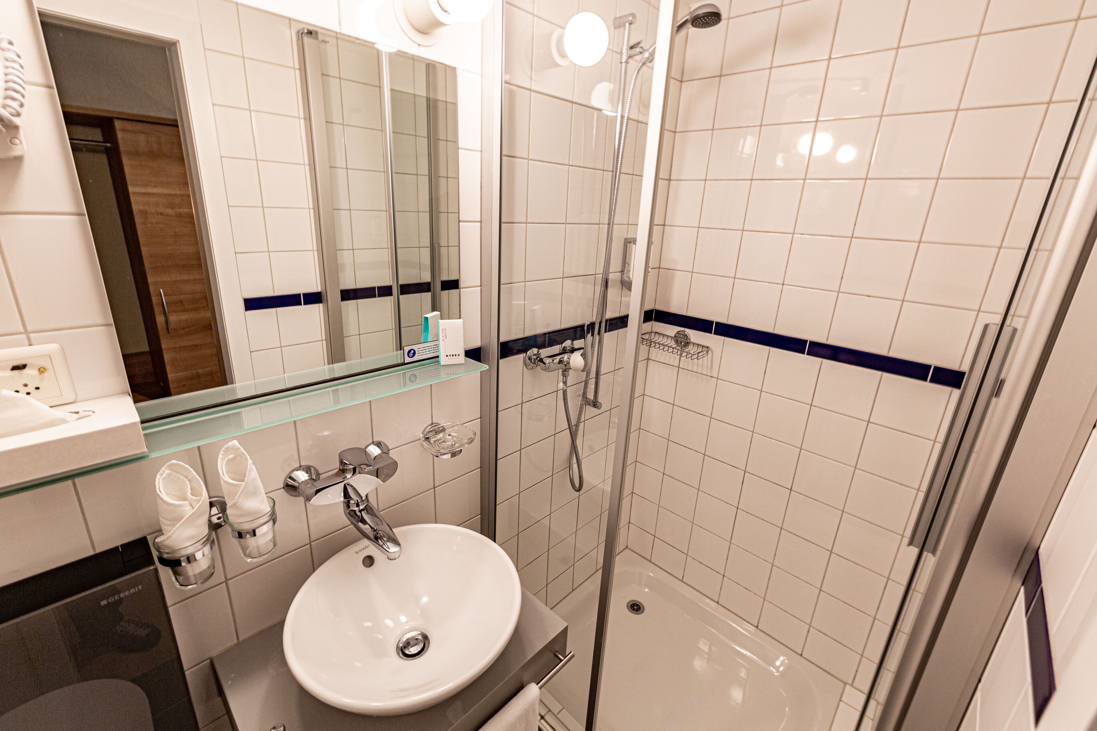 Ein modernes Badezimmer mit einer Duschkabine aus Glas, einem weißen Waschbecken und einem Spiegel darüber.
