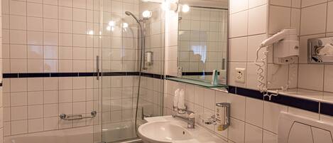 Une salle de bain moderne avec une douche à parois de verre, un lavabo avec un miroir et un sèche-cheveux posé sur le comptoir.