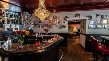 A bar area with a curved counter, a chandelier, and framed pictures on the wall.