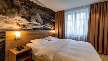 Ein Hotelzimmer mit einem großen Bett, einem Nachttisch mit Lampe und einer Wandmalerei einer Berglandschaft.