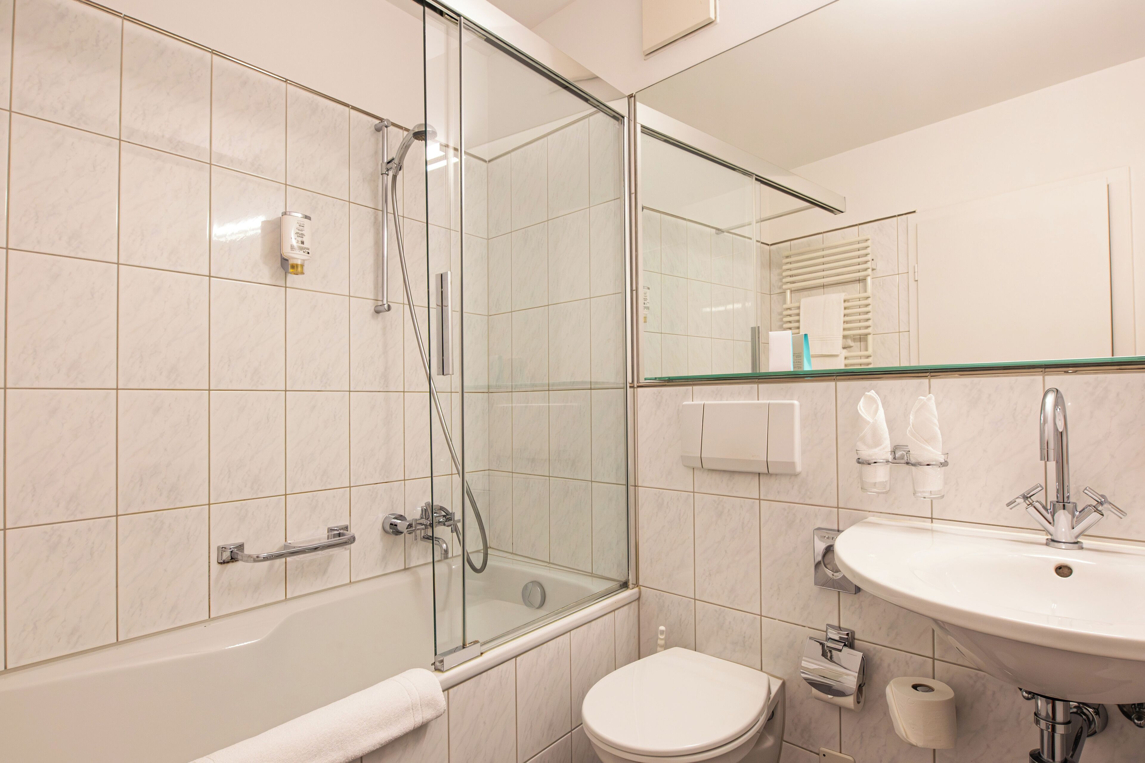 Et stilfuldt badeværelse med et glasafskærmet brusebad, et hvidt badekar, en vask og et toilet.