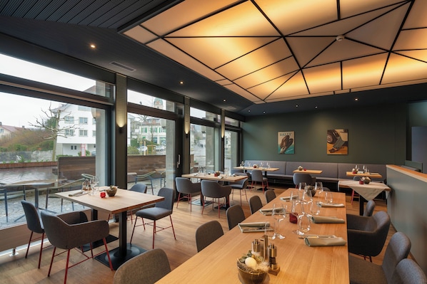 A modern restaurant with large windows, wooden tables, and contemporary chairs. - b_smart hotel Schönenwerd (Schonenwerd)