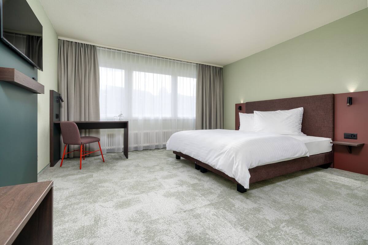 A hotel room with a bed, a desk, a chair, and a TV.