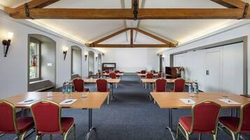 Une salle de conférence avec des tables et des chaises, des poutres en bois au plafond et un sol recouvert de moquette.