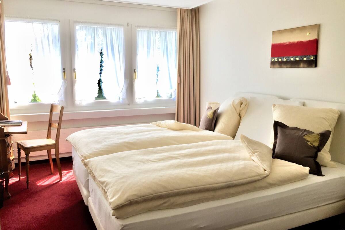 A hotel room with a large bed, a desk, and a window with curtains.
