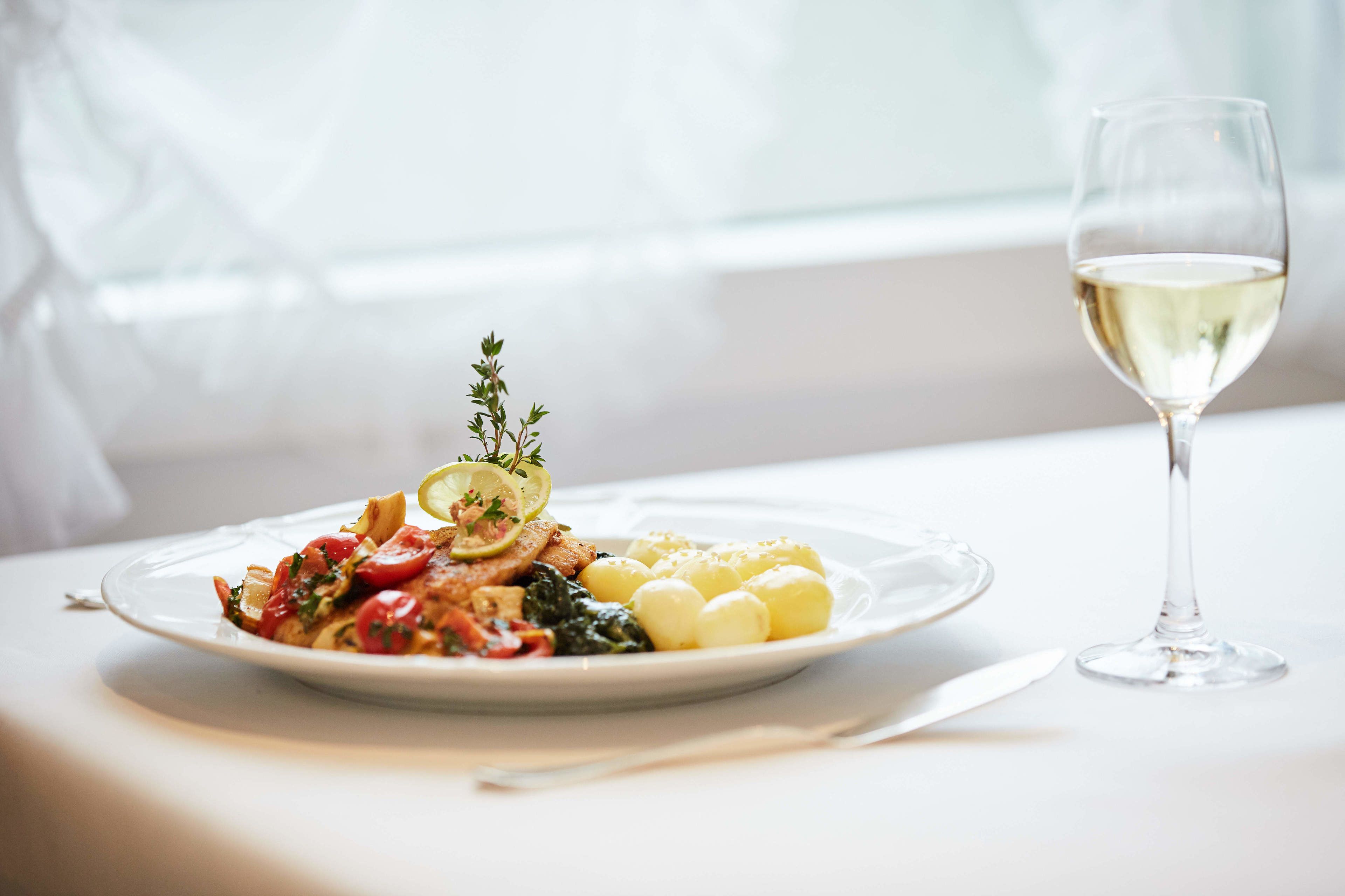 Un plato de comida con una copa de vino blanco sobre una mesa.