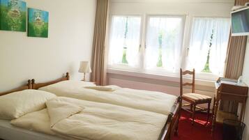 A hotel room with two beds, a desk, a chair, and a TV.