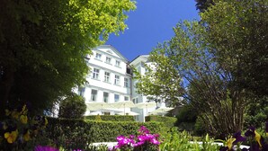 Un edificio con múltiples ventanas y un jardín bien cuidado con flores moradas y amarillas.