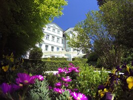 Un edificio con múltiples ventanas y un jardín bien cuidado con flores moradas y amarillas.
