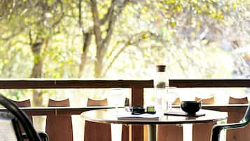 A round table with a bottle, glasses, and a bowl on a wooden deck with chairs.