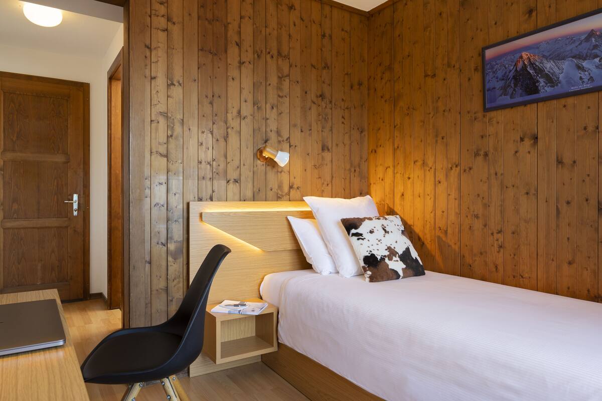 Une pièce aux murs lambrés, contenant un lit, un bureau et une chaise.