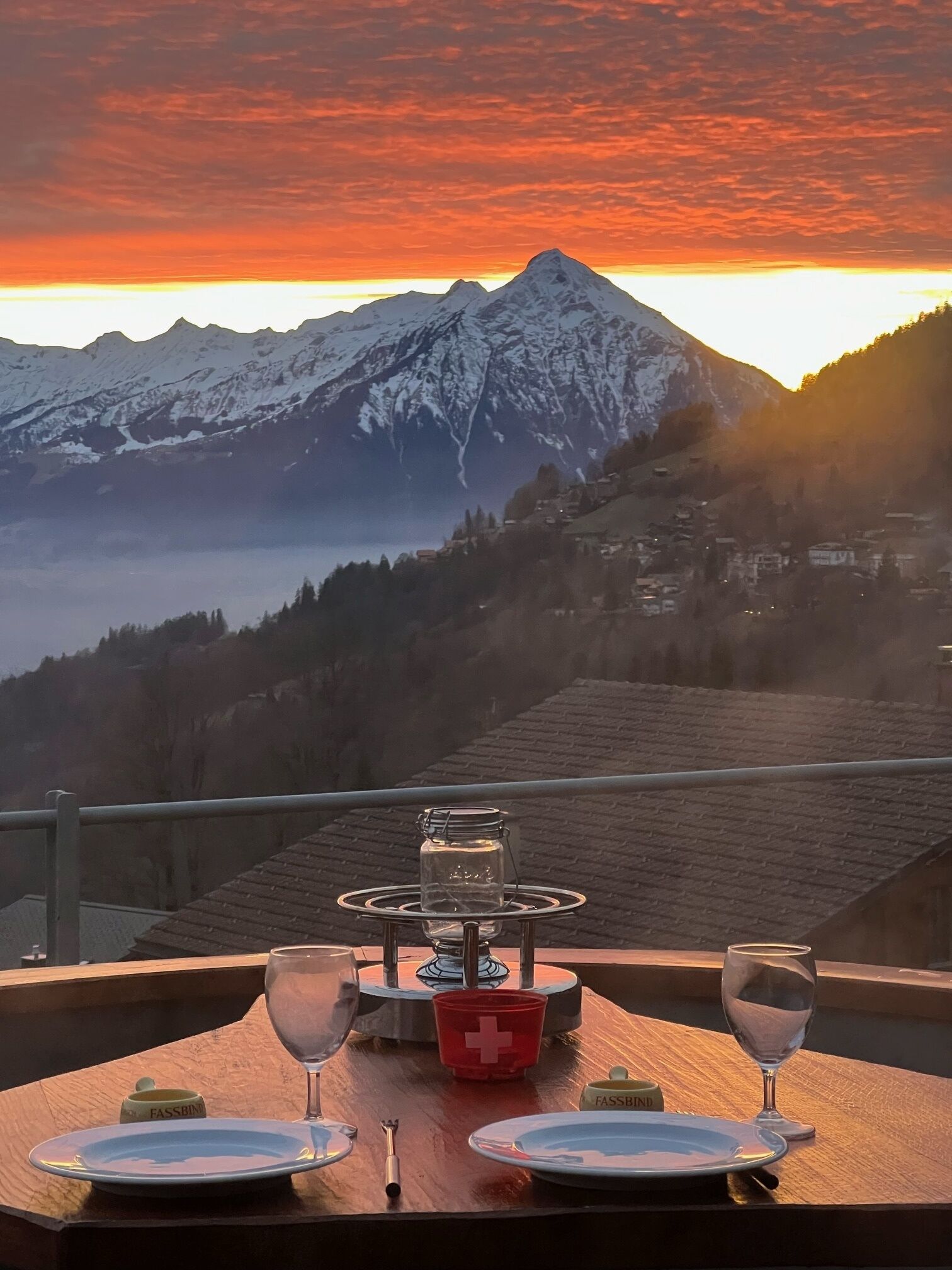 A table set for two with a view of snow-capped mountains and a sunset.