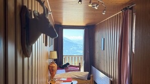 A wooden cabin room with a bed, a table with chairs, a lamp, and a deer head mounted on the wall. - Hotel Fassbind Beausite (Beatenberg)