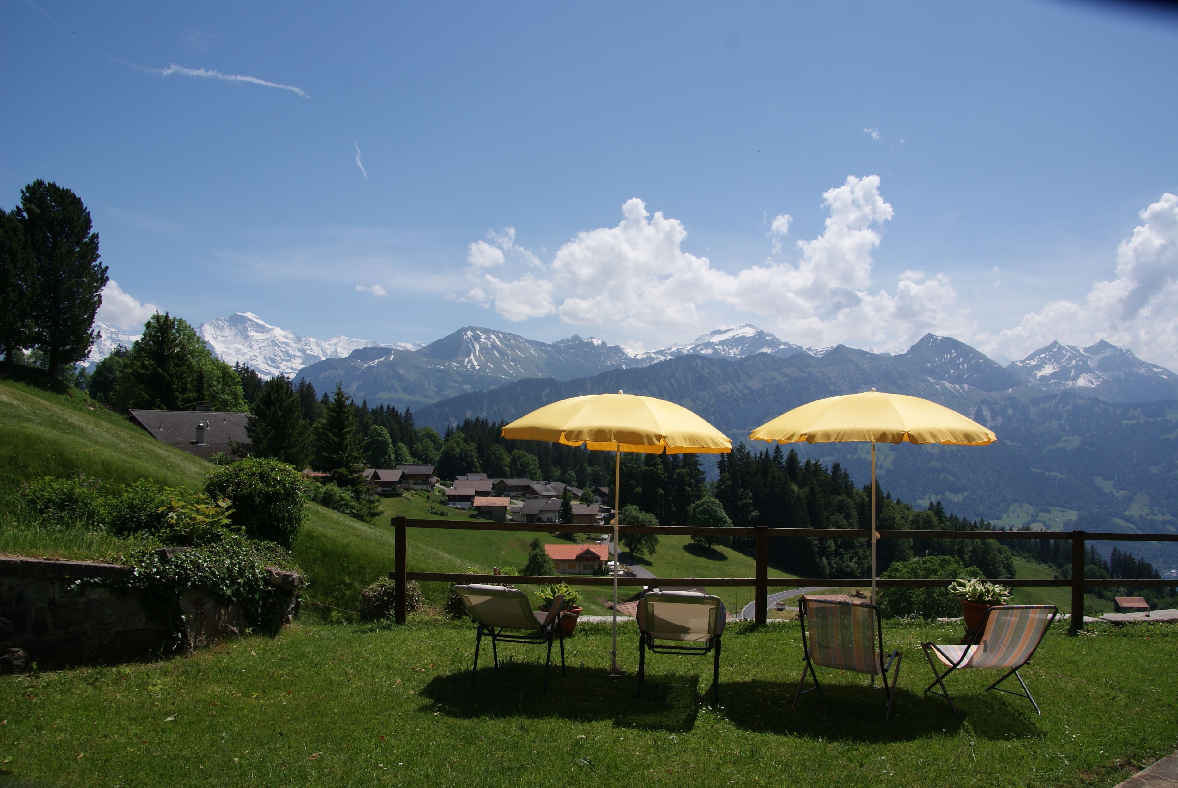 Una terraza con dos sombrillas amarillas, sillas y vistas a montañas nevadas.